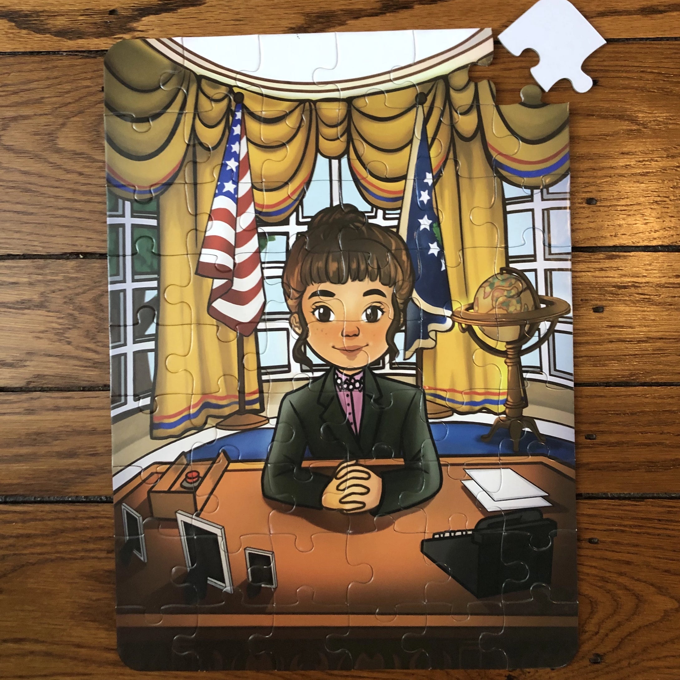 A completed jigsaw puzzle depicting a cartoon image of a girl sitting at a desk in the Oval Office, with American flags in the background. The puzzle is assembled from numerous pieces, placed on a wooden surface.